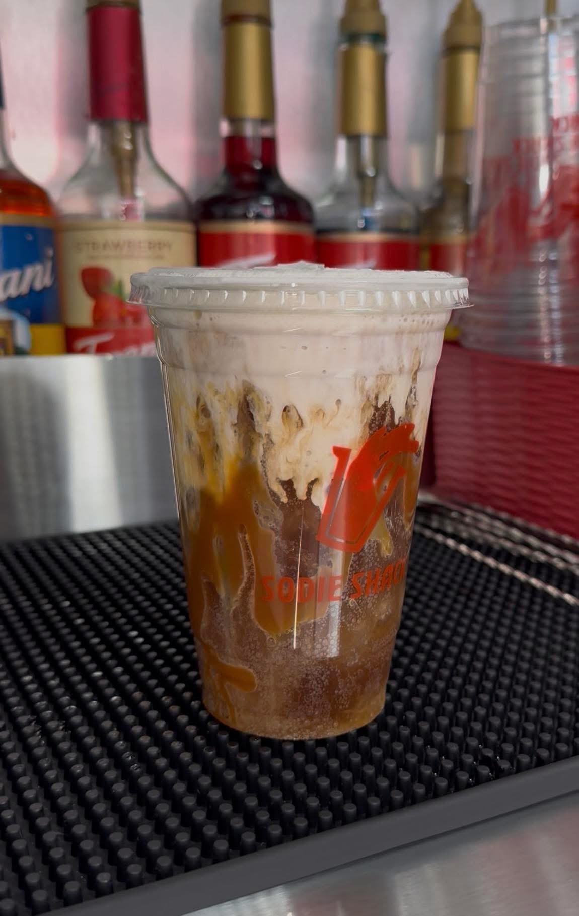 Caramel dirty soda topped with sweet cream foam in a Sodie Shack cup